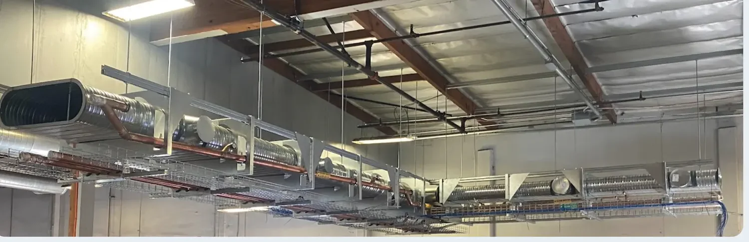 Installed multi-trade racks carrying oval duct, copper piping, and cable tray as one hung assembly