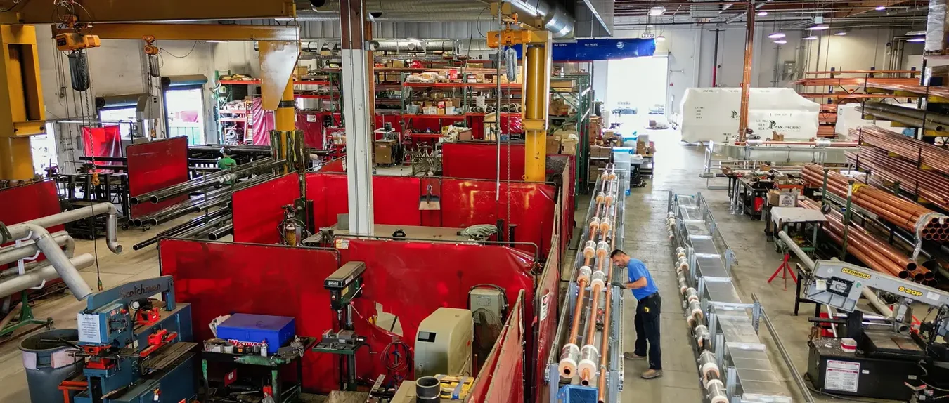Welding bays behind red screens beside a line of insulated copper rack assemblies in a Pan-Pacific shop