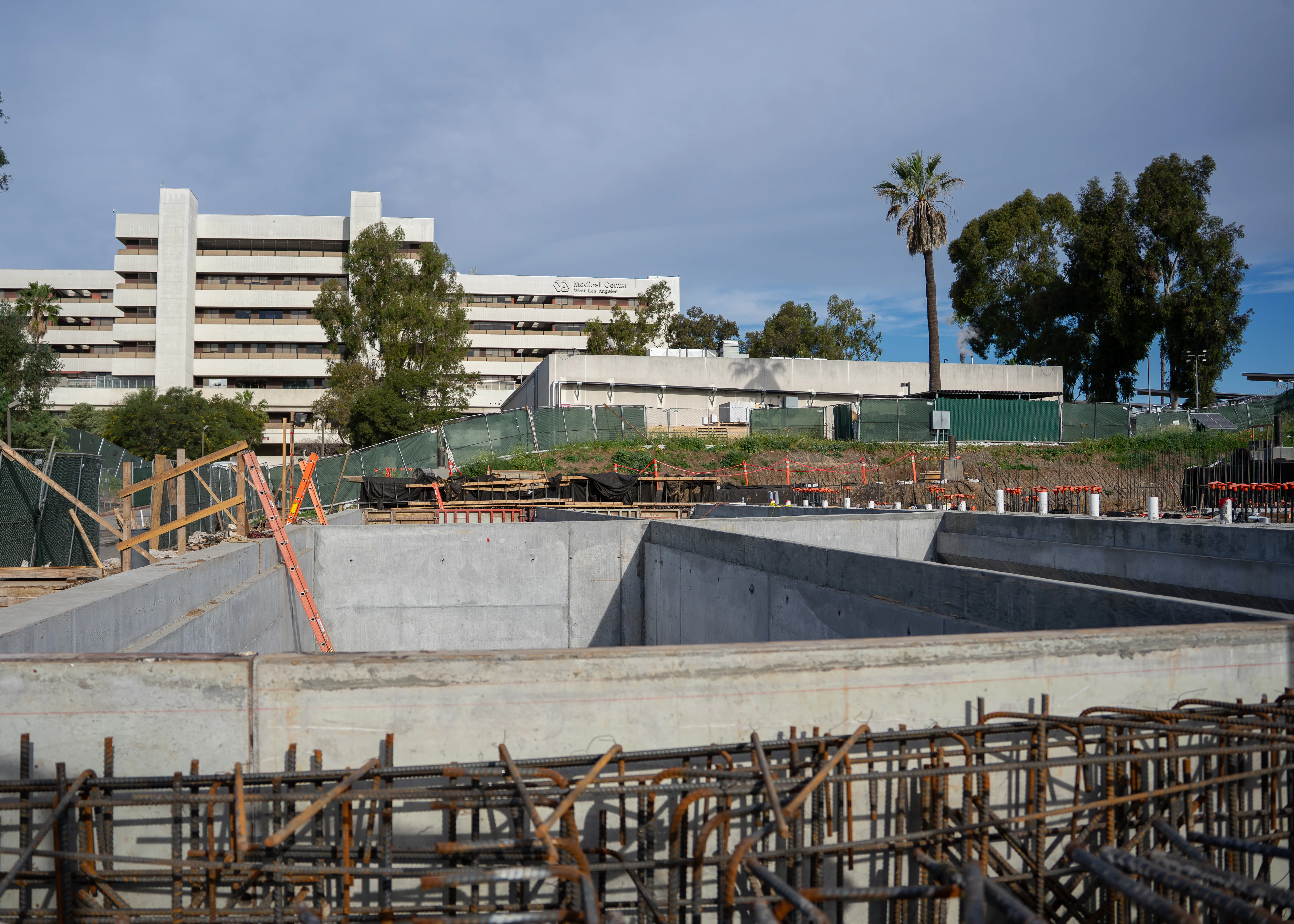 Concrete foundation and rebar for the new VA Medical Center building, with the existing hospital campus behind